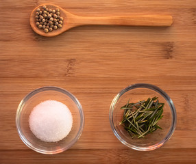 Crystal bowl with common marine salt, a wooden spoon with white peppercorns and rosemary on a wooden table