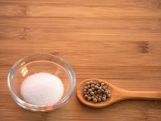 Crystal bowl with common marine salt and a wooden spoon with white peppercorns on a wooden table