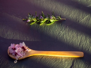 A wooden spoon with edible flowers and a rosemary twig on a slate plate