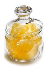 Dried pineapple candy rings, in powdered sugar, close-up under sunlight, lying in a transparent glass jar, on a white background.