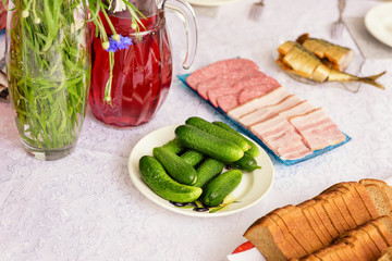 Salad Olivier. On white table is snack for vodka, in the form of fresh cucumbers, chopped smoked sausage and the cut bread lying in a separate plate.