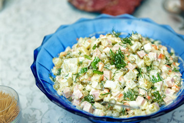 Salad Olivier. Russian salad with olive mayonnaise in a blue plate, on a white tablecloth.
