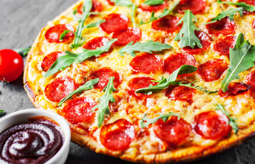 Pepperoni Pizza with Mozzarella cheese, salami, Tomatoes, pepper, Spices and Fresh arugula. Italian pizza on Dark grey black slate background
