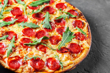 Pepperoni Pizza with Mozzarella cheese, salami, Tomatoes, pepper, Spices and Fresh arugula. Italian pizza on Dark grey black slate background