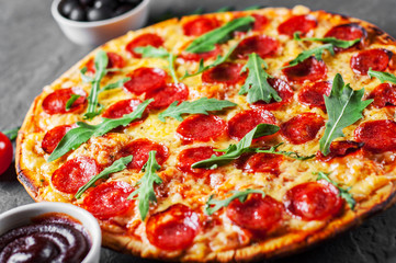 Pepperoni Pizza with Mozzarella cheese, salami, Tomatoes, pepper, Spices and Fresh arugula. Italian pizza on Dark grey black slate background