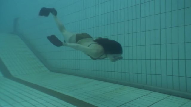Girl freediver swims in flippers underwater in swimming pool. Young woman freediver swims underwater in freediving training.