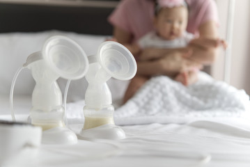 Breast milk in milk pump's bottles and pump machine on the bed with mother hugging baby in background. The milk got from milk pump's machine and ready for the baby. Baby health care concept