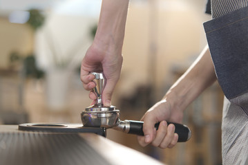 Close up view of barista tamping grinded coffee bean in the coffee tamp on tamp mat before put into the coffee making machine. Seen from side view in the restaurant. Barista and coffee making concept.