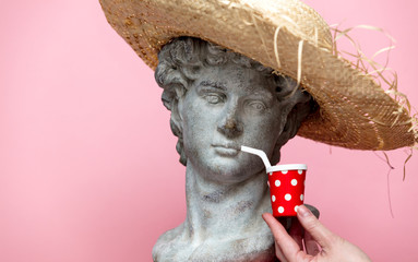 Antique bust of male in hat with cola drink on pink background.