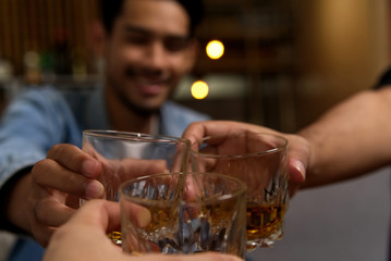 Close up shot of glasses clinking between group of friends drinking whiskey at night party in...