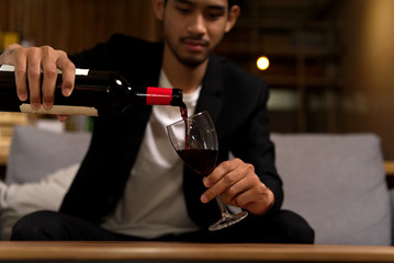 Luxury alcohol drinking. Close up shot of man in suit sitting on sofa pouring the wine in wine glass at home. He pays attention on the wine level in the glass to make it perfectly.