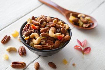 Mix nuts and dried fruits background and wallpaper. Seen in top view of mix nuts and dried fruits in the bowl and wood spoon decorated with some nuts and red leaf on white wood in background.