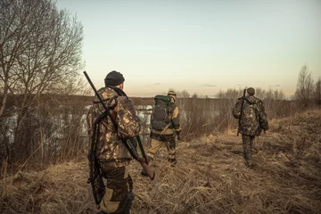 Poster Im Rahmen Jagdszene mit einer Gruppe von Jägern mit Jagdmunition, die während der Jagdsaison bei Sonnenuntergang durch ländliches Feld geht © splendens