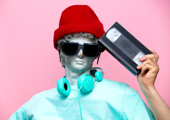 Antique bust of male in hat with headphones and VHS cassette