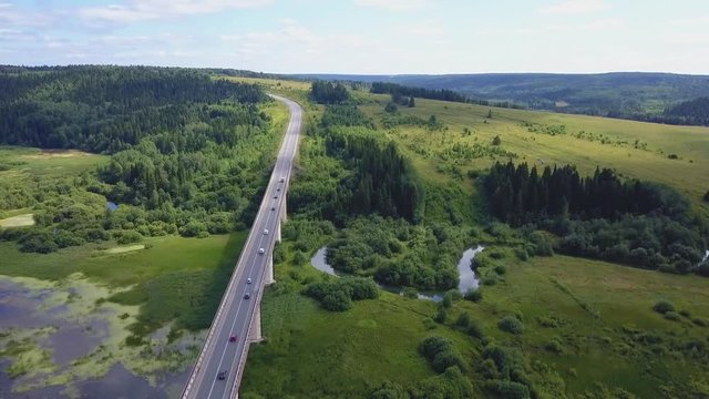 Aerial view of a busy bridge road with moving cars crossing a swamp with water and valley. Clip. Cars moving.