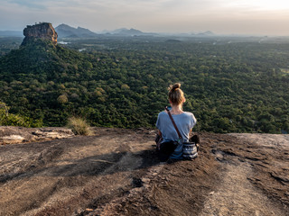 Naklejka premium Young caucasian woman sitting on the top of the Rock Pidurangala. Sri Lanka, March 10, 2019.