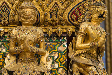 Obraz premium Golden guardian demon statues at the base of a golden Chedi at Bangkok Grand Palace in Thailand