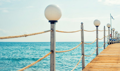 Wooden pier with lamp and cord railing against blue sky and sea background. Tropical landscape