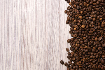 Roasted coffee beans in bulk on a light wooden background. dark cofee roasted grain flavor aroma cafe, natural coffe shop background, top view from above, copy space
