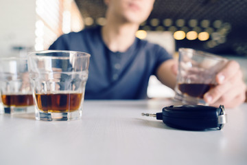 Close up on car keys on the table with a man holding a glass of whiskey alcohol in the background drinking and driving
