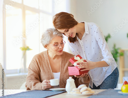 Happy mother's day! adult daughter gives gift  and congratulates an elderly mother on holiday .