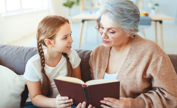 happy family grandmother reading to granddaughter book at home