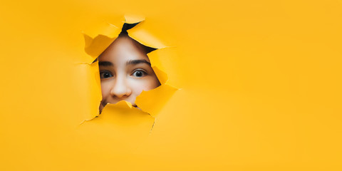 Surprised teenage caucasian girl face. Cute attractive girl looking through hole. Copy space for advertising, to insert text or slogan. Discount, sale.