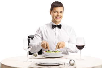 Handsome man eating a salad at a restaurant table and smiling at the camera
