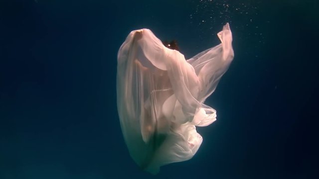 Birth of an angel in creation of underwater model freediver. Creativity and art of creating images on background of clear transparent blue water of sea. Young woman in white cloth.