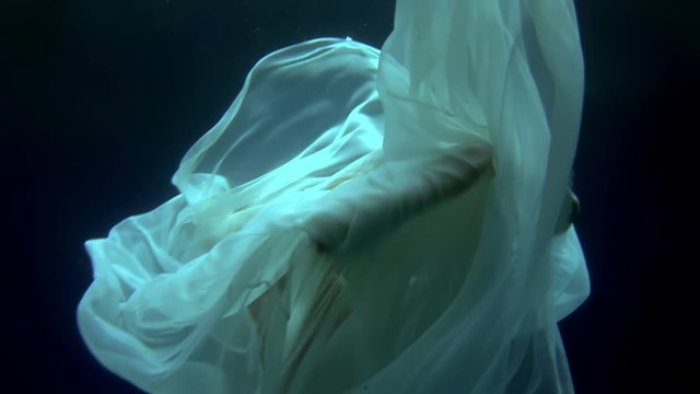 Young woman underwater model freediver depicts birth of an angel. Creativity and art of creating images on background of clear transparent blue water of sea.