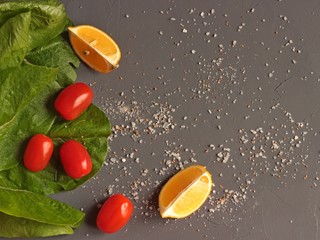 Cherry tomatoes on a dark background. Lettuce leaves, lemon slices and scattered salt.