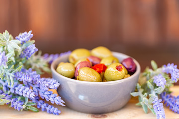Olives stuffed with red pepper and herbs spices. Multi-colored olives in a small bowl on a wooden table. Lavender. Blurry background. Closeup. Soft focus. Copy space.