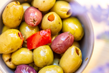 Olives stuffed with red pepper and spices of herbs. Multi-colored olives in a gray bowl on a rustic table. Blurry background. Macro. Image doesn’t in focus. Top view.