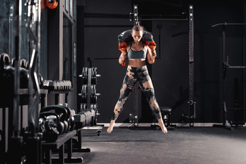 Fototapeta na wymiar Full length of Caucasian female bodybuilder jumping with bulgarian sack on shoulders. Night workout in gym concept.