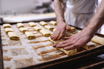 Caucasian baker in white uniform putting pastry on baking tray. Bakery interior.