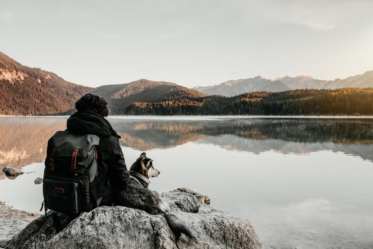 Mensch und Hund auf der Reise genießen Freundschaft am einsamen See mit Ausblick auf die Berge bei Sonnenaufgang