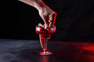 guy hand keeps a little snake near a glass with red liquid in the dark room