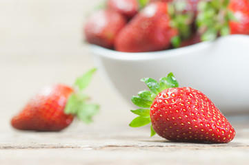 Fresh ripe organic strawberry fruit in white bowl on white wooden background, close up harvested strawberries concept