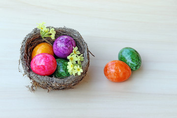 Ein Osternest mit bunten Ostereiern und Schlüsselblumen auf Holzuntergrund