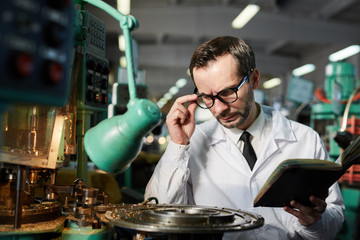 Portrait of mature quality inspector wearing lab coat checking industrial machine units in factory workshop, copy space