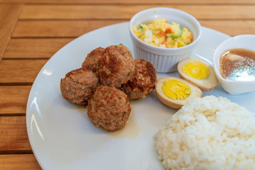 Japanese homemade style meatballs with stream rice , boiled egg and mash potato salad on white plate and wooden table.