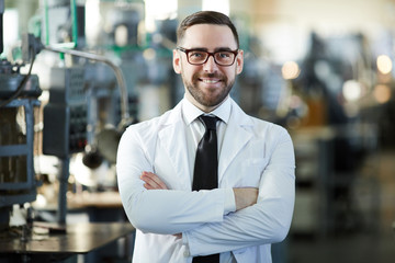 Waist up portrait of handsome factory worker wearing lab coat posing confidently in workshop and...