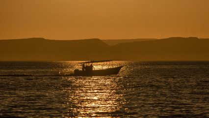 A boat slips between the water and the sun on its way back to port in La Paz Mexico.
