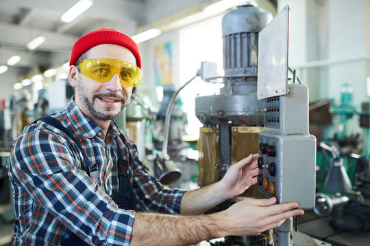 Portrait of smiling factory worker looking at camera while operating machine units in workshop, copy space