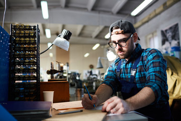 Portrait of modern factory worker taking notes sitting at table in workshop, copy space