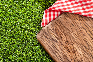 Chopping board and red checkered napkin on the green grass.