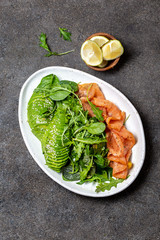 Low carbs salad. Spinach, rucola salad with avocado and salmon. Black concrete background, white plate, top view