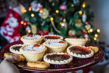 Hand holding plate with cookies, tartlets and tarts, blurred christmas tree on background.