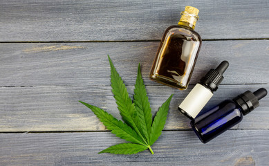 Hemp leaf on wooden background, cannabis oil extracts in bottles