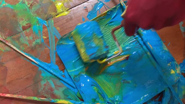 Paint roller rolls through blue green plaint